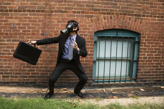 Businessman standing next to brick wall wearing gas mask in fighting stance.