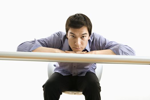 Young Asian business man with head on desk looking at viewer.