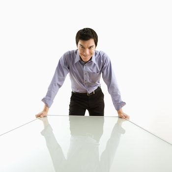 Young Asian business man standing over conference table with devilish grin.