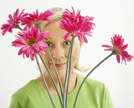 Portrait of smiling adult blonde woman looking through bouquet of pink flowers at viewer.