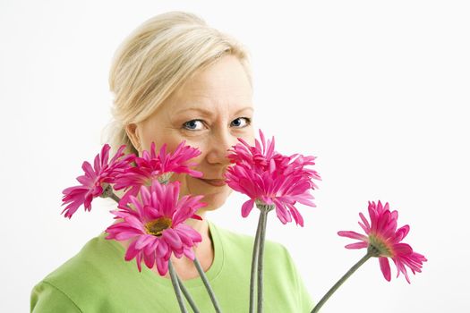 Portrait of smiling adult blonde woman looking over bouquet of pink flowers at viewer.