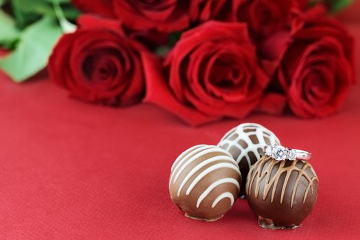 Diamond engagement sitting on chocolate truffles with red roses. Selective focus on diamond ring with soft blurred background.
