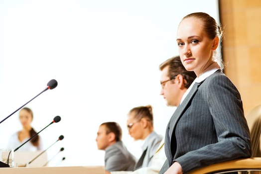 group of business people sitting at the tables at the presentation, woman looking at the camera