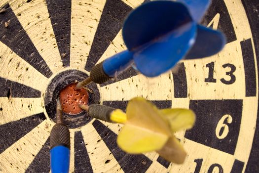 Old dartboard with a blue and a yellow plastic dart.