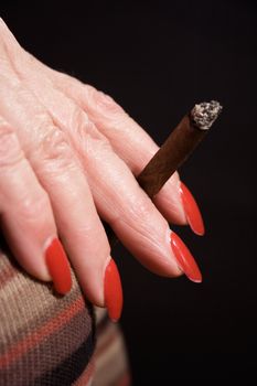 Mature woman holding a small cigar. Isolated on a black background.