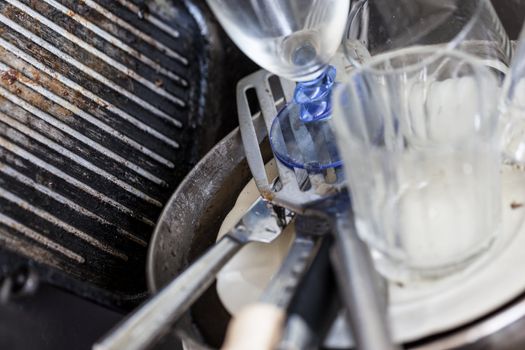 a lot of dirty pans, glasses and other kitchen utensils in a sink