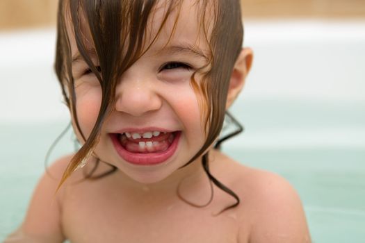 Squeezed eyed, teething toddler girl  giving a big laugh with wet hair.