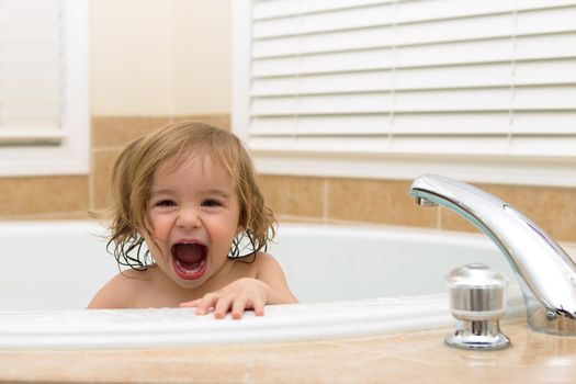 Toddler girl laughing cheerfully her moth open from bath tub. Teething