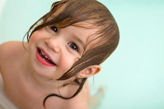 Cute Toddler girl giving happy trusty smile from the bath tub with her wet hair.