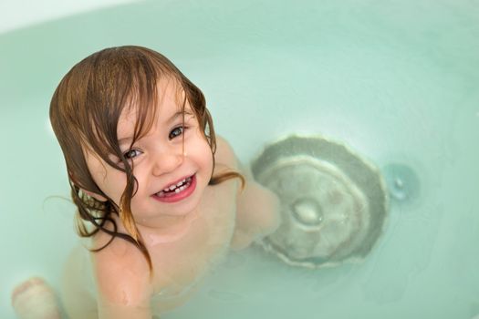 Cute Toddler girl giving toothy smile from the bath tub,