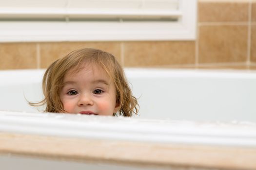toddler girl giving happy hiding look from the bathtub, perhaps she is looking to take her bath.