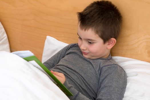 Eight years old reading his book in the bed before he goes to sleep.