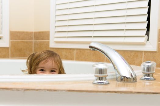 Toddler girl giving happy hiding look from the bathtub, perhaps she does not want to take a bath