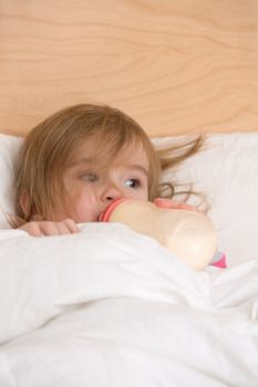 Cute toddler getting nutritious milk before goes to sleep under the blanket.