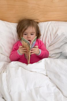 Reading habits starts with early age, cute toddler is just browsing the pages in her pink pajamas before she goes to sleep.