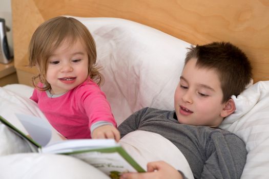 Little sister pointing a page to his older brother in the book before they go to sleep.