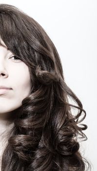 Studio portrait of a seductive young woman with beautiful long wavy brunette hair peering around the edge of the frame with one eye looking at the camera, high key