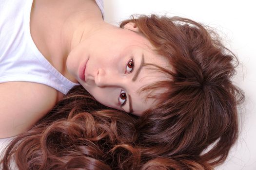 Beautiful serious young woman lying on her back with her lovely curly brunette hair spread around her face looking up at the camera