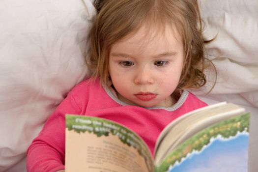 Cute Ttoddler reading her stories before she goes to sleep. Reading habits starts with early age.