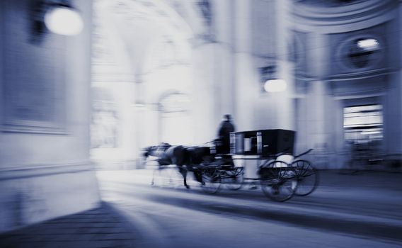 One of the famous horse cabs of Vienna, Austria driving though the gateway of Hofburg Castle. Intentional motion blur in capture to reflect action.