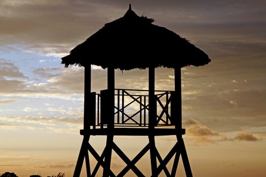 Tropical watchtower overlooking a beach silhouette at sunset