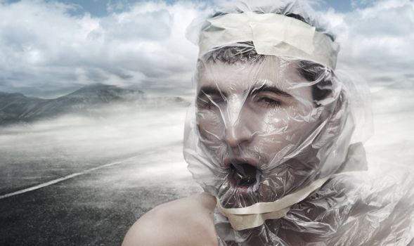 Young man in the desert with a bag on his head trying to breathe