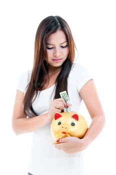 Portrait of a pretty young woman putting money into piggy bank over white background.