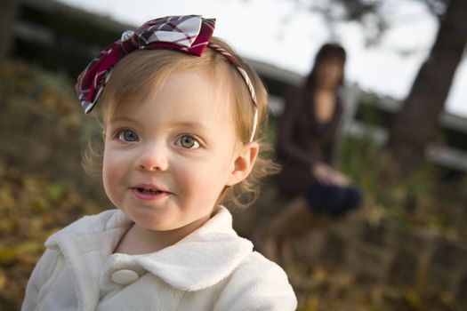 Adorable Baby Girl Playing Outside in the Park with Mom Behind Her.