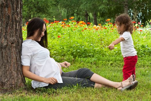 Young pregnant woman and her little baby girl in a summer garden