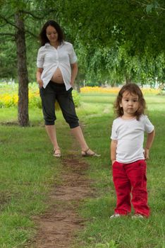 Young pregnant woman and her little baby girl in a summer garden