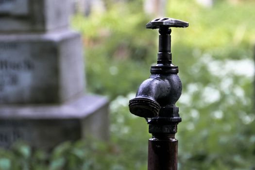 A lone faucet in an Austrian cemetery with dripping water in front of a tombstone