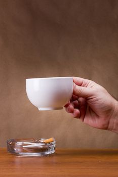 Hand holding a cup and a cigarette ashtray.