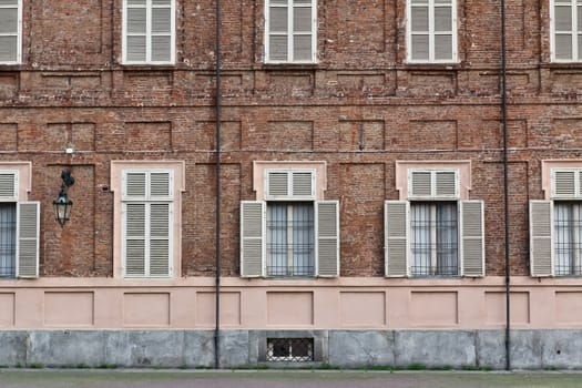 A facade of a brick building with white wooden windows on a square in Torino