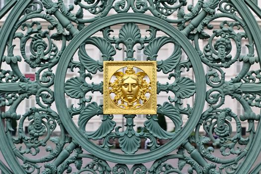 A green fence with a skillful metal pattern including a golden element in front of a palace in Torino
