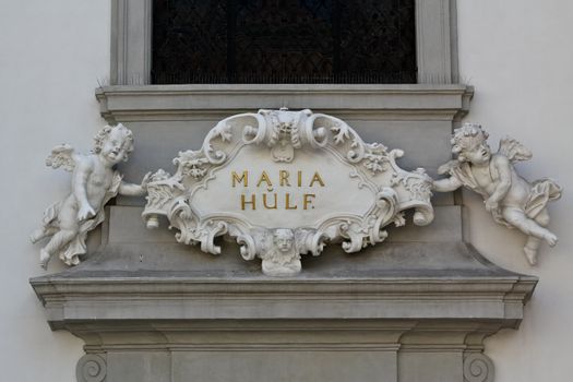 A baroque shield held by angels on a church in the city of Vienna indicating the name of the district "mary help"