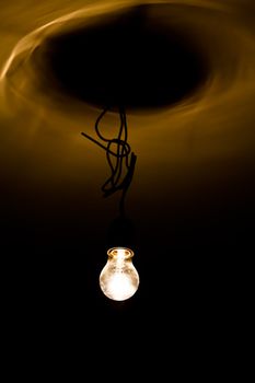 A bulb shining in the dark on a wire throwing orange reflections on the ceiling