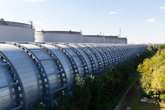 A noise barrier of a road from behind next to an industrial area with silos