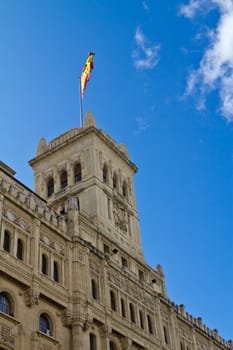 An ancient spanish building with the national flag on it