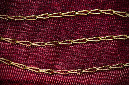 A red cloth texture with strong contrast and lines with golden decorative chains.