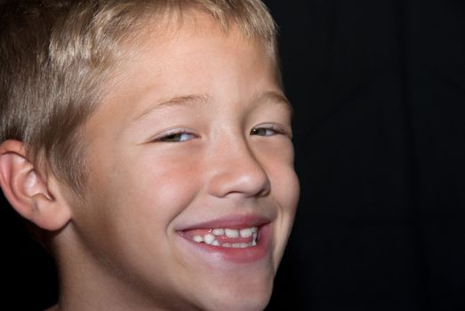 Smiling and happy young blonde boy on black background.