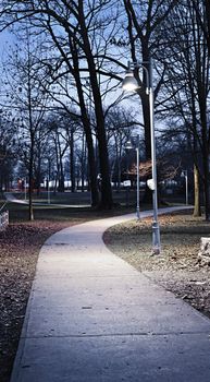 Path through city park at dusk with street lamps