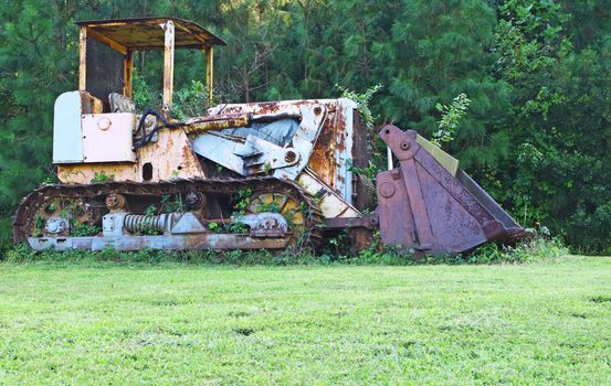 A high contrast picture of an antique vintage old and rusted weed and plant overgrown Bulldozer in a field outside.