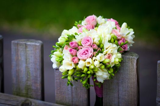Wedding bouquet with roses and freesia on rustic country fence