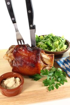 fresh Pork hock with mustard, lettuce and parsley on a board with cutlery