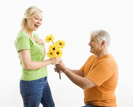 Middle-aged man on bended knee giving woman bouquet of yellow flowers.