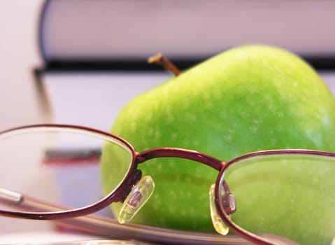 green apple with books and eyeglasses