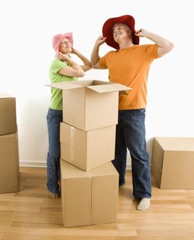Middle-aged couple trying on silly hats while packing or unpacking moving boxes.
