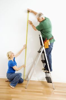 Middle-aged couple measuring wall with tape.