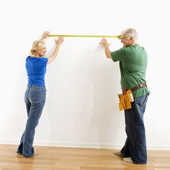 Middle-aged couple measuring wall with tape.