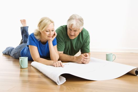 Middle-aged couple lying on floor looking at architectural blueprints together.